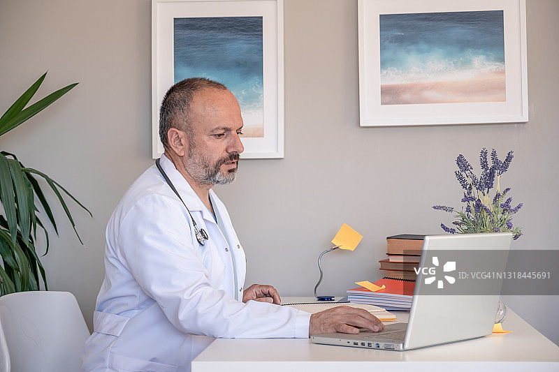 远程医疗。高级医生坐在家庭办公室用笔记本电脑与患者进行在线视频咨询。图片素材
