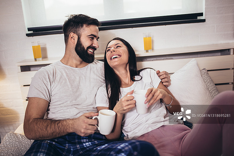可爱的情侣在卧室里吃早餐喝咖啡。图片素材