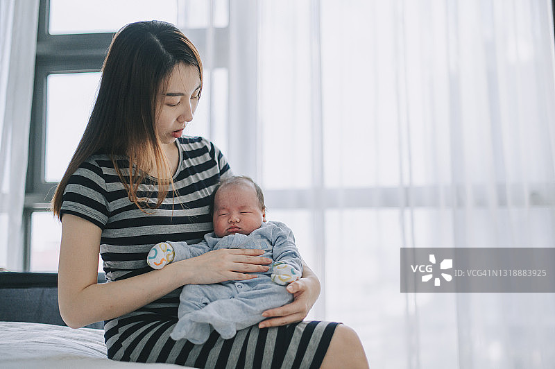 一位年轻的亚裔华人母亲抱着她的男婴在卧室里图片素材