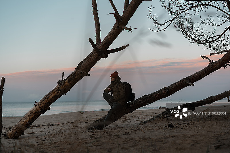 海滩放松。年轻人看着海面上的夕阳。站在芦苇间的沙丘上图片素材