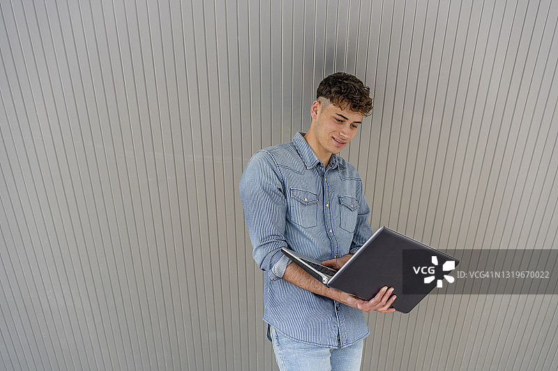 一个年轻人站在墙前使用笔记本电脑图片素材