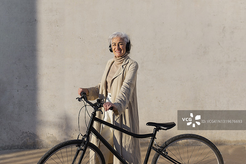微笑的成熟女人戴着耳机站在自行车上图片素材