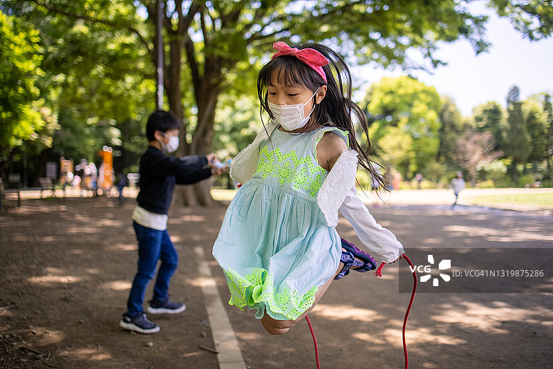 戴着防护面罩的小女孩在公园里跳绳图片素材