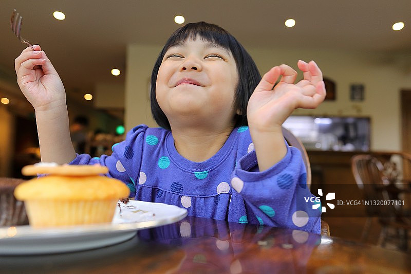可爱的小女孩闭着眼睛微笑，对纸杯蛋糕甜点很满意图片素材