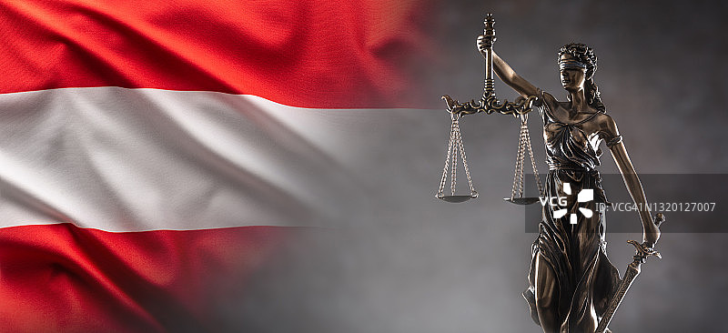 正义是一尊象征法律的盲人雕像，手中握着天平和宝剑，背景是一面奥地利国旗。图片素材