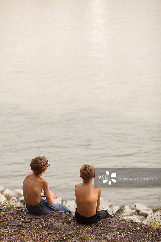 男孩们悠闲地坐在海边，欣赏着河的景色图片素材