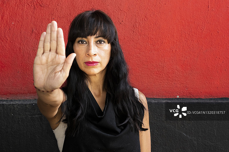 拉丁美洲妇女看着摄像机和手势停止，红色和黑色的背景图片素材