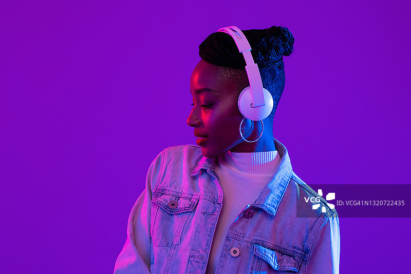 年轻的非洲裔美国妇女戴着耳机听未来主义紫色赛博朋克霓虹灯光背景音乐图片素材