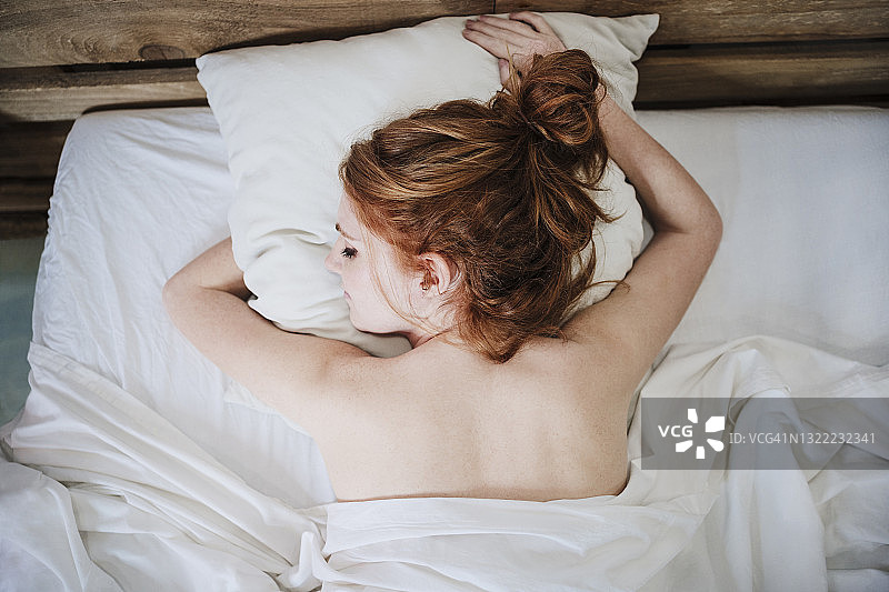 一个红头发的年轻女人睡在家里的床上图片素材