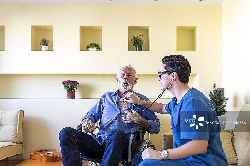男医生正在照顾一位老人的家访和检查他的医疗条件与听诊器。图片素材