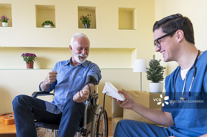 一位年轻医生在家为一位坐轮椅的老人测量血压。图片素材