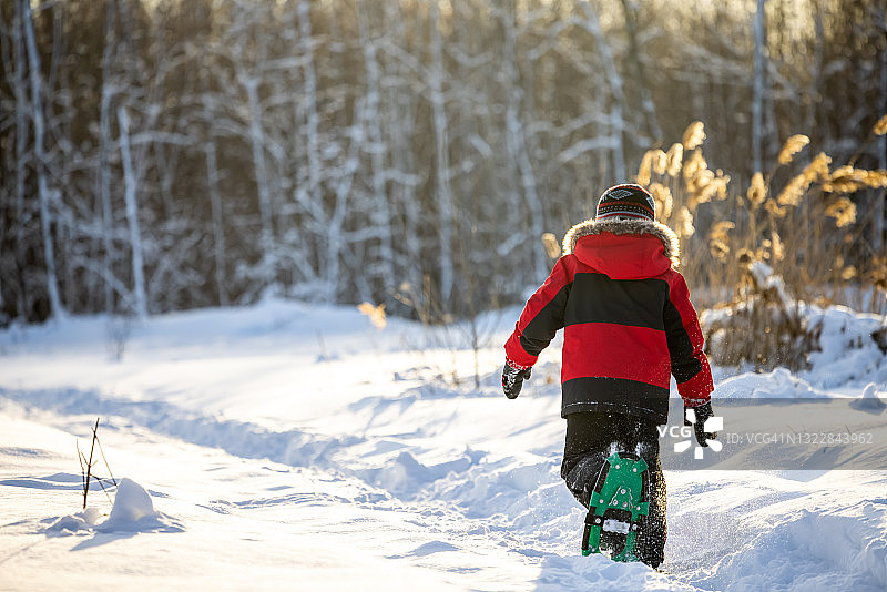 在冬天日落时分，小男孩在户外的粉末雪中穿雪鞋图片素材