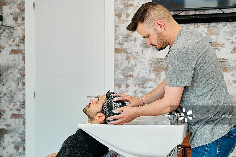 一个理发师在给一个年轻人理发之前在理发店洗头的侧视图。图片素材