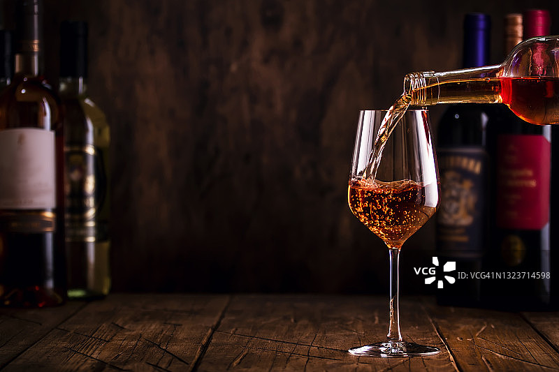 品酒。在木制背景下，将玫瑰葡萄酒倒入玻璃杯中，酒瓶中可选择红、白、玫瑰葡萄酒图片素材