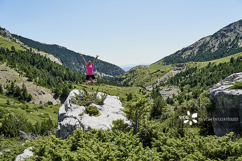 一名年轻女子在山中徒步旅行后在岩石顶端跳图片素材