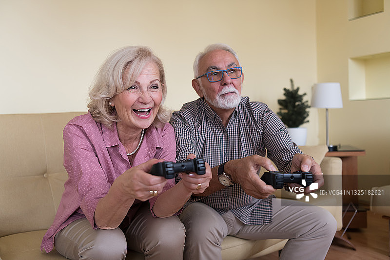 微笑的老人和他美丽的妻子在家里一起玩电子游戏。图片素材