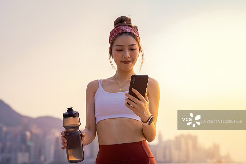 年轻的亚洲女运动员会在智能手机应用上查看自己的健身数据，以监控自己早上在城市里锻炼后的锻炼进度。青年文化。积极的生活方式。健康健身与科技理念图片素材