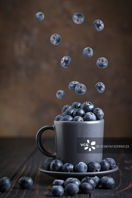 新鲜的生蓝莓落在空气中孤立在黄色的背景。食物悬浮的概念。蓝莓放在篮子里，背景是黑色。图片素材