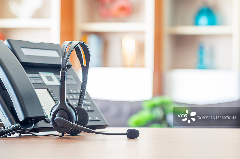 近距离软聚焦耳机与电话设备在办公桌客户服务支持。VOIP耳机用于客户服务支持(呼叫中心)的概念。图片素材