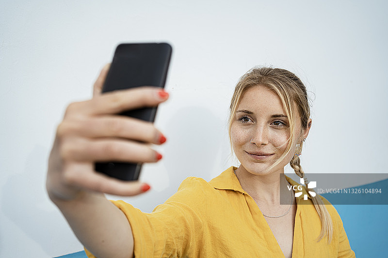 微笑的女人通过手机在白色墙壁自拍图片素材