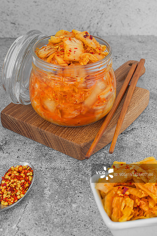 韩国人自制的辛辣食物泡菜在一个玻璃罐和沙拉碗与筷子在灰色的背景。健康益生菌素食概念。图片素材