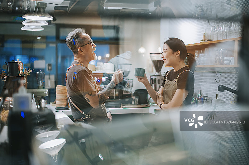 亚洲华人资深男性咖啡店老板和她的女儿倚着喝咖啡休息和聊天在咖啡店柜台图片素材