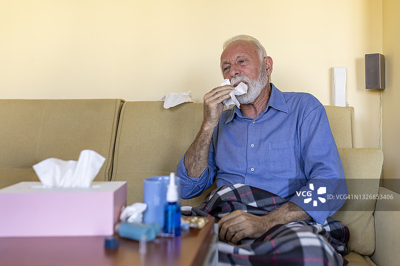感冒老人躺在家里对着纸巾打喷嚏图片素材