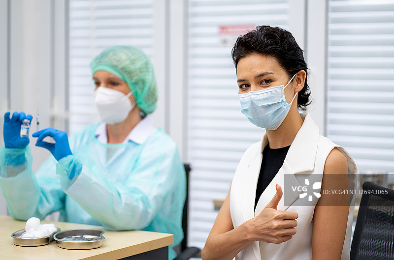 一名戴口罩的年轻女子在注射Covid-19疫苗后，对着摄像机竖起大拇指图片素材