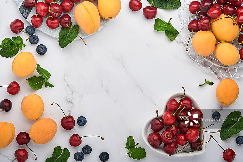 白色大理石背景上点缀着新鲜的杏、红樱桃和黑莓。素食、减肥、清洁健康的饮食理念。前视图。副本的空间。图片素材