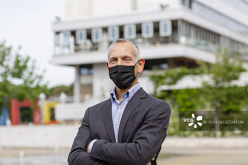 2019冠状病毒病期间，在城市建筑附近佩戴防护口罩的商人图片素材