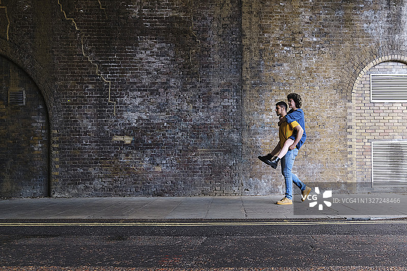 年轻男子背着女友走在人行道上图片素材