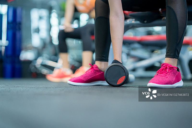 近距离的运动女性从健身房里的地板上拿起哑铃。图片素材