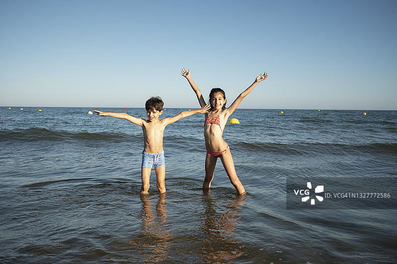 快乐的女孩和男孩在海滩上举起双手图片素材