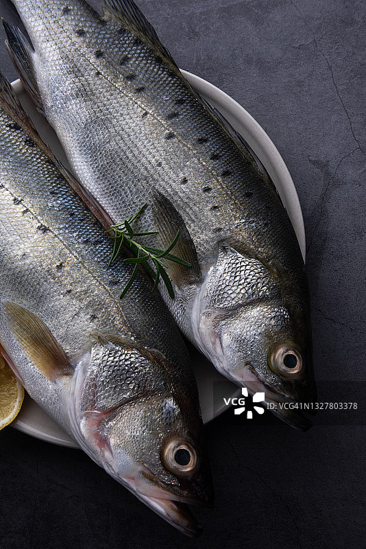 新鲜的生鲈鱼与迷迭香和柠檬在黑暗的背景图片素材