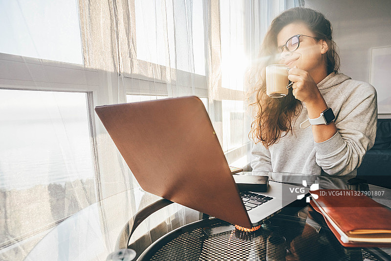 职场女性坐在桌子对面的笔记本电脑和喝咖啡。图片素材