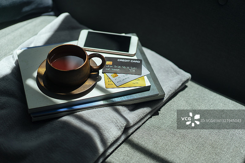 把木制咖啡杯、信用卡和智能手机放在舒适的沙发床上图片素材