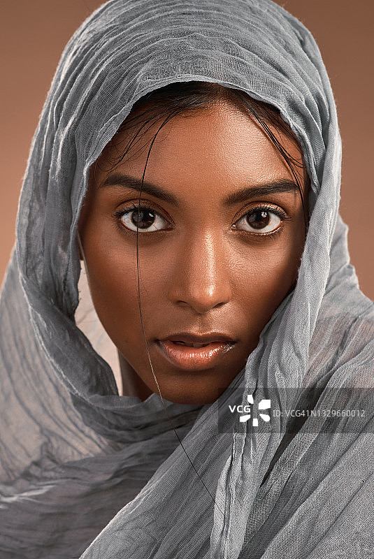 一个迷人的年轻女子的肖像戴着头巾，以棕色的背景图片素材