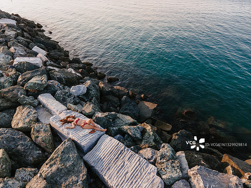 在海边的岩石上做日光浴的女人图片素材