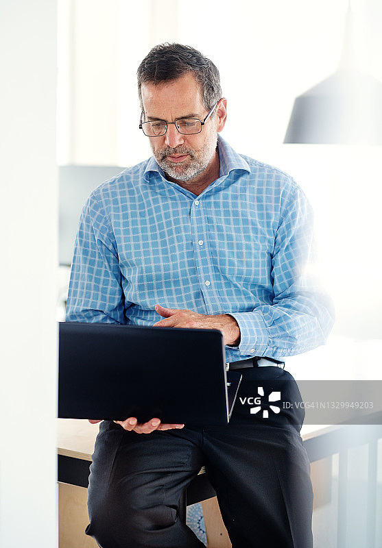 一个成熟的商人靠在办公桌上用笔记本电脑图片素材