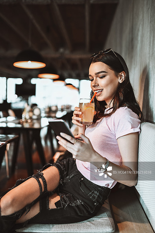 现代女性美容使用智能手机和喝柠檬水在餐厅图片素材