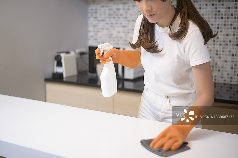 年轻漂亮的女人戴着防护橡胶手套在家里的厨房清理桌子。图片素材