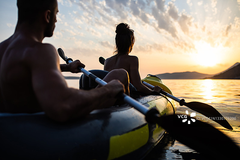 一对夫妇在海边划独木舟，享受浪漫的日落图片素材