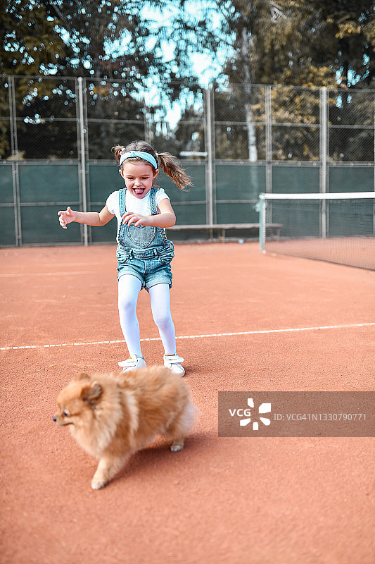 网球场上微笑的女孩追着博美犬图片素材