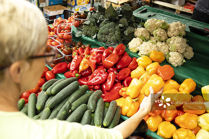 年长白种人妇女在市场购买新鲜有机蔬菜和水果，手里拿着满满一袋健康食品的俯视图。图片素材