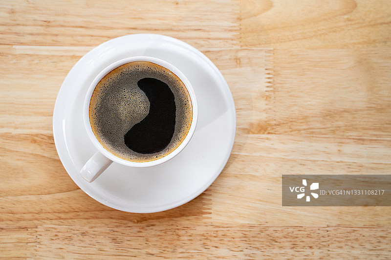 一杯咖啡放在木桌上。杯咖啡与心的图案在一个白色的杯子上木制背景图片素材
