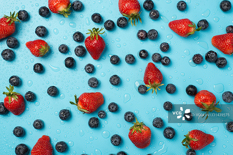 上面的照片是一堆蓝莓，草莓到处都是，蓝色背景上孤立的水滴图片素材