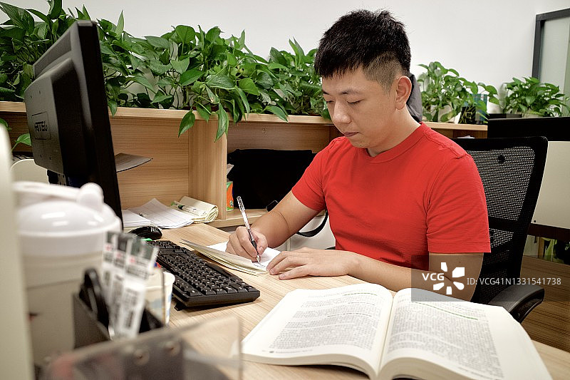 一个年轻人正在书桌前写作。图片素材