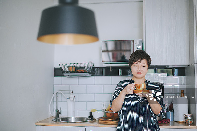 亚洲的中国成熟女性在厨房休息喝咖啡早餐，在清新的早晨上班前提神醒脑图片素材