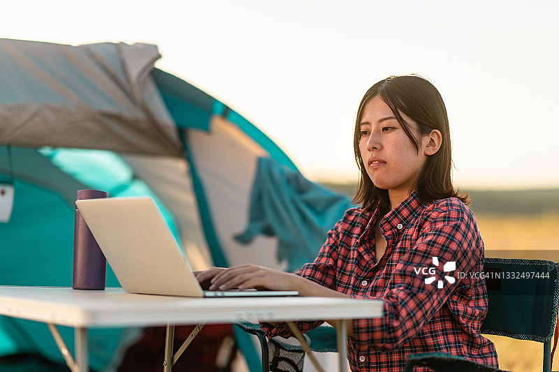在野外露营时，一名年轻女子在帐篷旁使用笔记本电脑图片素材