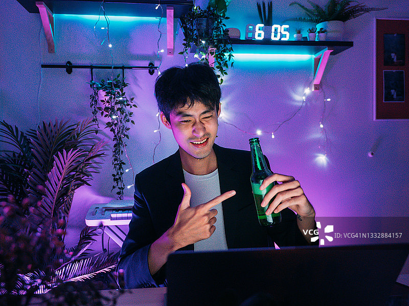 一个亚洲男人在家里开视频会议，喝着啤酒。图片素材